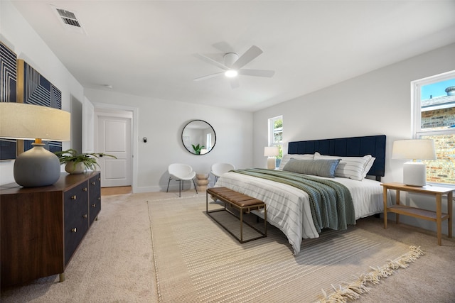 bedroom featuring a ceiling fan, light colored carpet, visible vents, and multiple windows