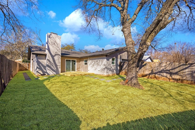 rear view of property with a fenced backyard, a yard, and a chimney