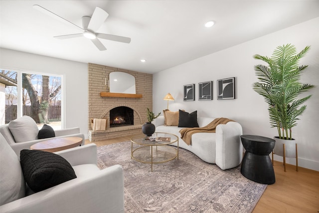 living area featuring light wood finished floors, recessed lighting, a brick fireplace, ceiling fan, and baseboards