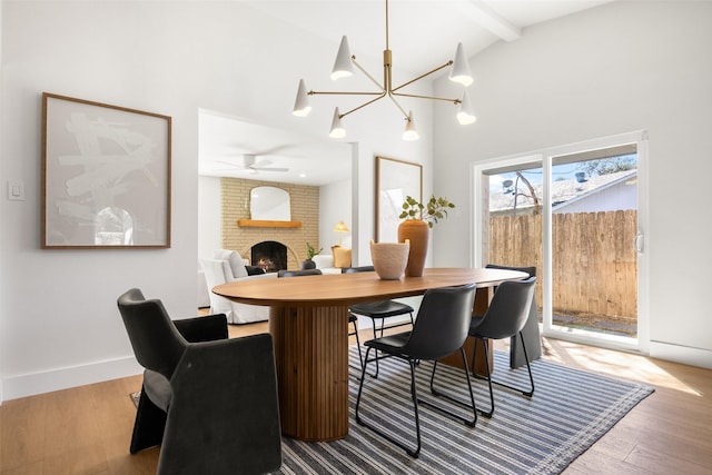 dining space featuring high vaulted ceiling, a fireplace, wood finished floors, baseboards, and beamed ceiling