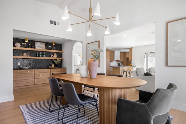 dining area featuring arched walkways, baseboards, visible vents, and light wood-style floors