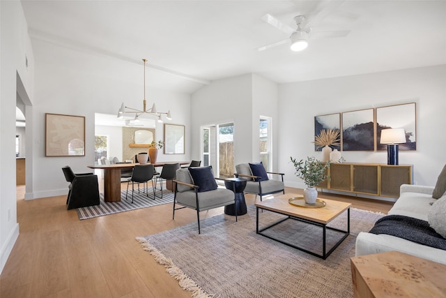 living room with high vaulted ceiling, ceiling fan with notable chandelier, baseboards, and wood finished floors