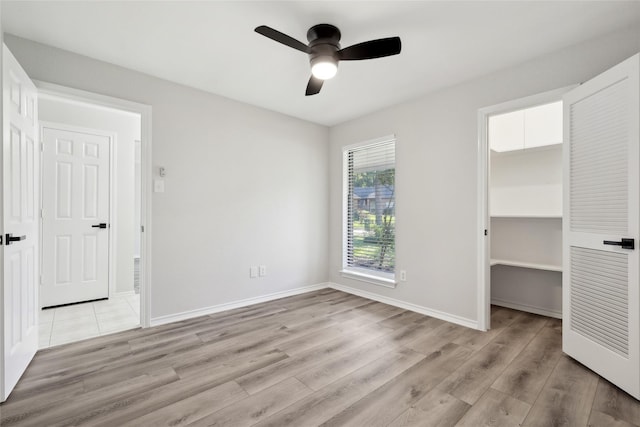 unfurnished bedroom featuring a walk in closet, light wood finished floors, a closet, ceiling fan, and baseboards