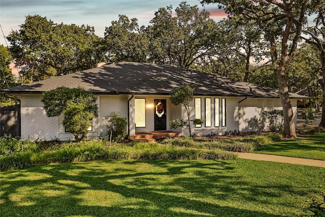 view of front of home featuring a yard, roof with shingles, and brick siding