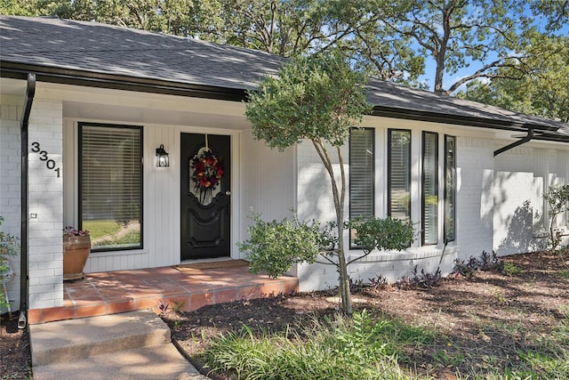 entrance to property featuring a shingled roof, covered porch, and brick siding