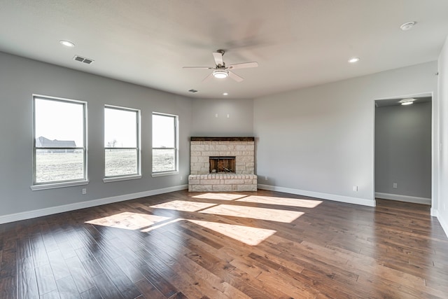 unfurnished living room with baseboards, visible vents, dark wood-type flooring, and a stone fireplace