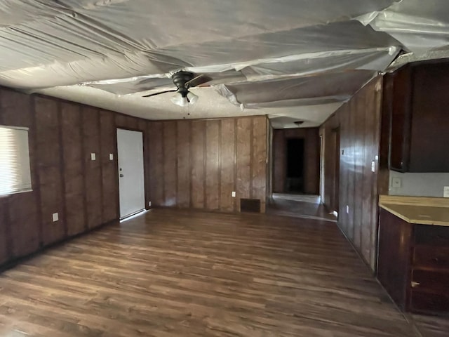 unfurnished living room with dark wood finished floors, a ceiling fan, and wooden walls