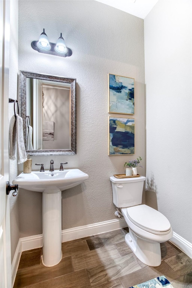 half bathroom with baseboards, toilet, and wood finished floors