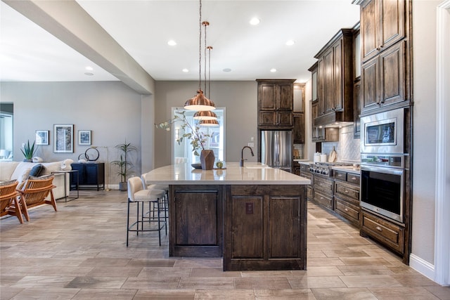 kitchen featuring stainless steel appliances, light countertops, open floor plan, dark brown cabinetry, and a sink