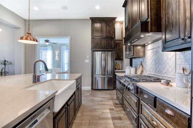 kitchen featuring dark brown cabinetry, decorative backsplash, decorative light fixtures, stainless steel appliances, and a sink