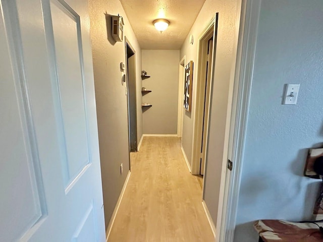 hallway featuring light wood-style floors, baseboards, and a textured wall