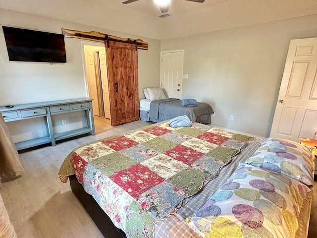 bedroom with ceiling fan, a barn door, wood finished floors, and visible vents