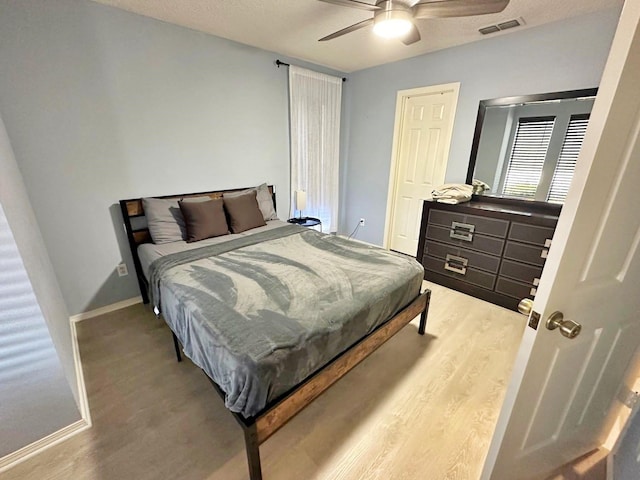 bedroom with a textured ceiling, wood finished floors, a ceiling fan, visible vents, and baseboards