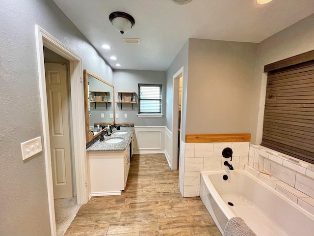 full bathroom featuring a wainscoted wall, wood finished floors, vanity, visible vents, and a bath