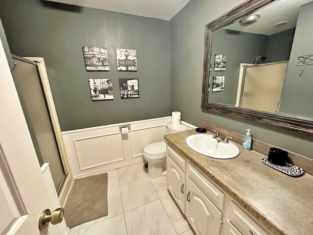 bathroom featuring toilet, vanity, marble finish floor, wainscoting, and a shower stall