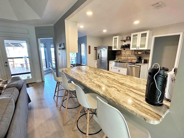 kitchen with visible vents, white cabinets, a breakfast bar, wood finished floors, and stainless steel appliances