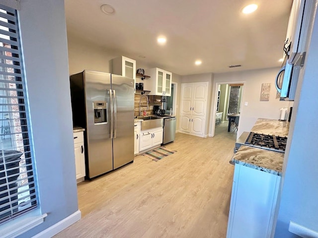 kitchen with appliances with stainless steel finishes, white cabinetry, light wood-style floors, and a sink