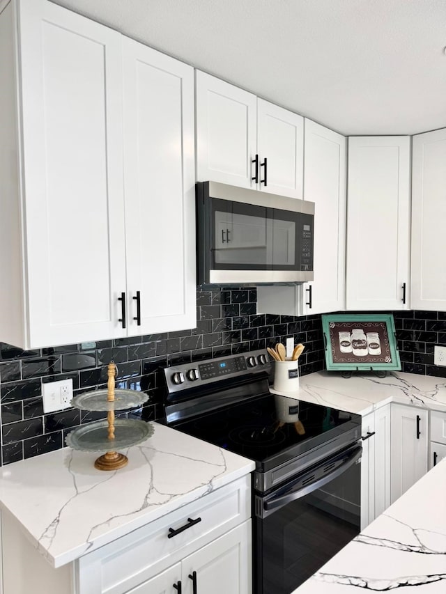 kitchen with tasteful backsplash, white cabinets, electric stove, light stone counters, and stainless steel microwave