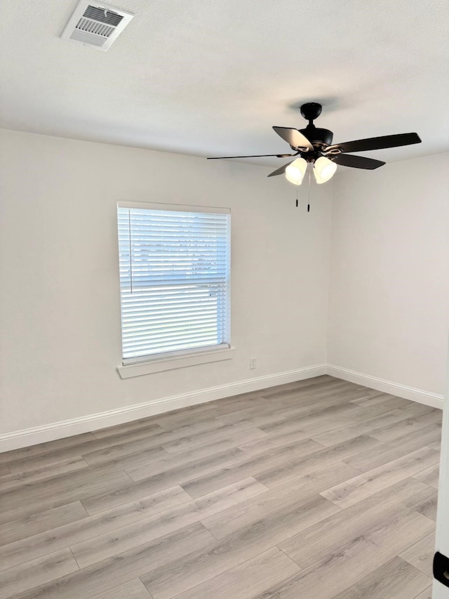 spare room featuring light wood-type flooring, visible vents, and baseboards