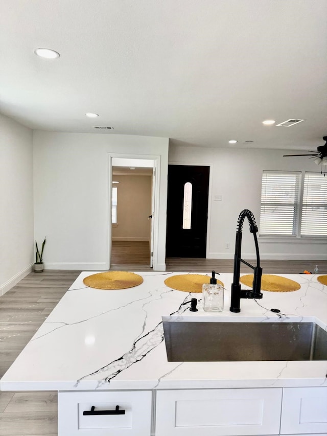 kitchen featuring light stone counters, visible vents, light wood-style floors, white cabinets, and a sink