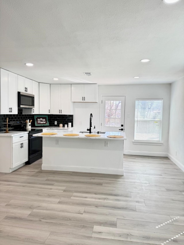 kitchen with tasteful backsplash, stainless steel microwave, electric range, white cabinetry, and a sink