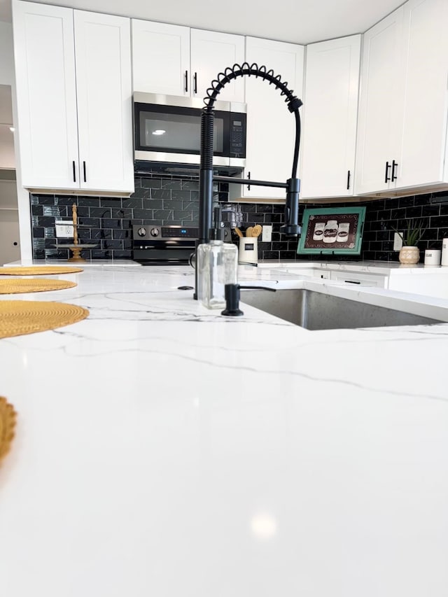 kitchen with stainless steel appliances, decorative backsplash, white cabinetry, and light stone countertops