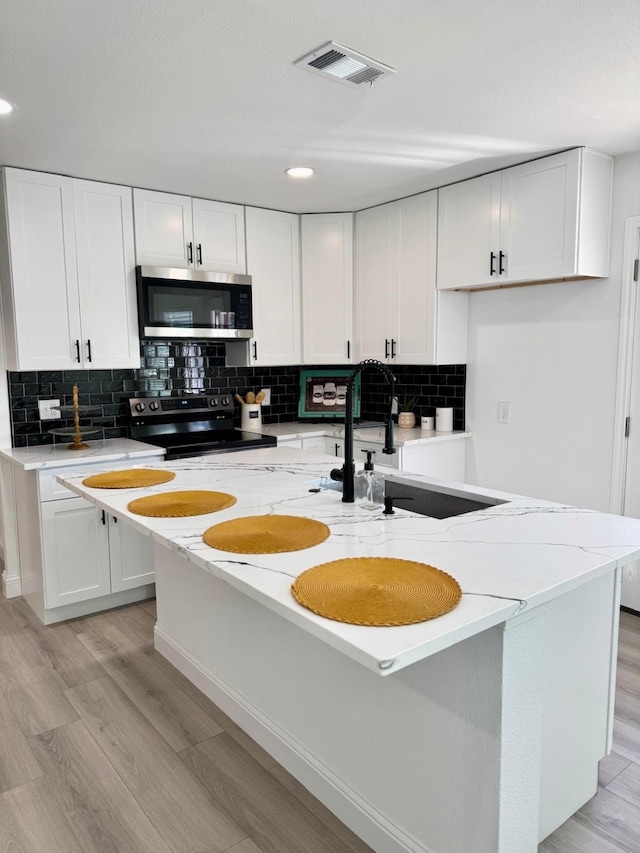 kitchen with visible vents, stainless steel microwave, electric range, a sink, and light stone countertops