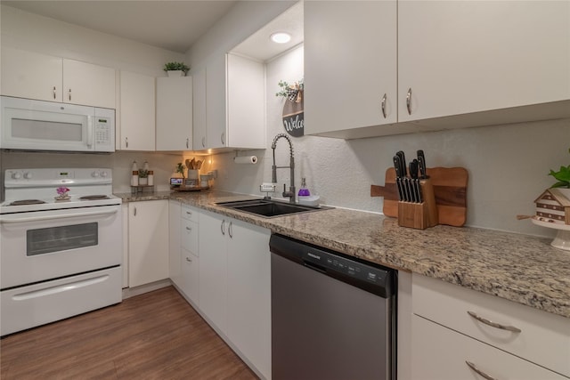 kitchen featuring white appliances, wood finished floors, a sink, white cabinetry, and decorative backsplash