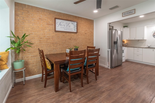 dining room with brick wall, dark wood finished floors, a ceiling fan, and baseboards