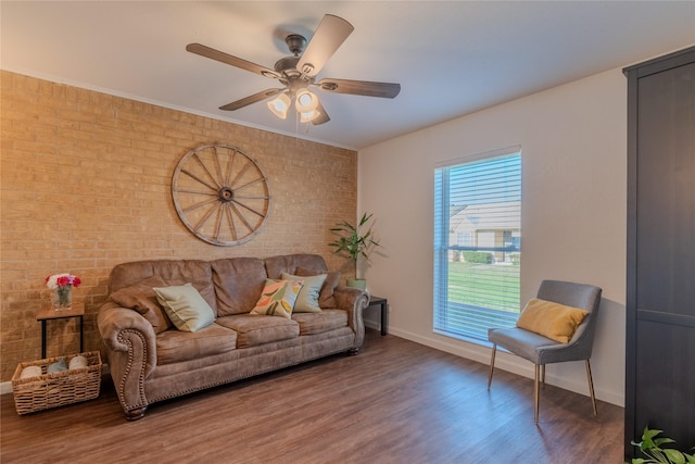 living area featuring baseboards, brick wall, ceiling fan, ornamental molding, and wood finished floors