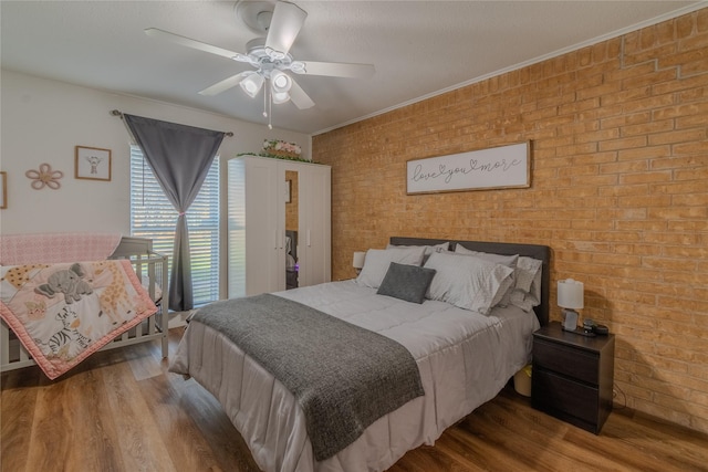 bedroom featuring brick wall, wood finished floors, a ceiling fan, and crown molding