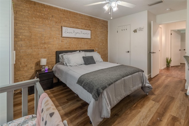 bedroom featuring visible vents, ceiling fan, brick wall, and wood finished floors