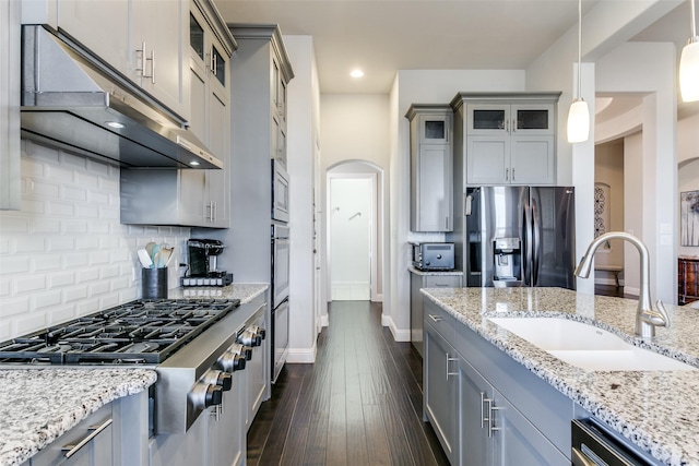 kitchen featuring arched walkways, stainless steel appliances, gray cabinetry, a sink, and under cabinet range hood