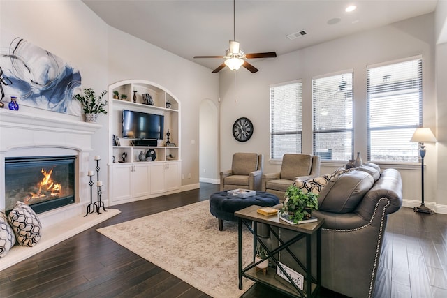 living area featuring dark wood-style floors, a high end fireplace, visible vents, and built in features