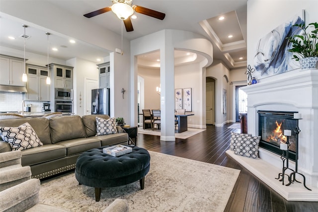 living room featuring baseboards, arched walkways, dark wood finished floors, a glass covered fireplace, and recessed lighting