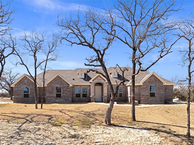 french country style house with roof with shingles and brick siding