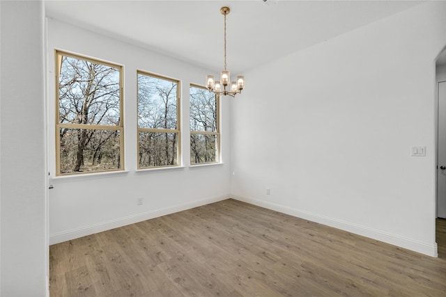 spare room featuring a chandelier, baseboards, and wood finished floors