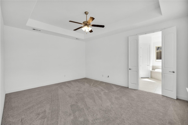 unfurnished room featuring a tray ceiling, carpet flooring, ceiling fan, and visible vents