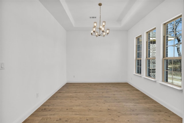 interior space with a tray ceiling, visible vents, baseboards, and wood finished floors