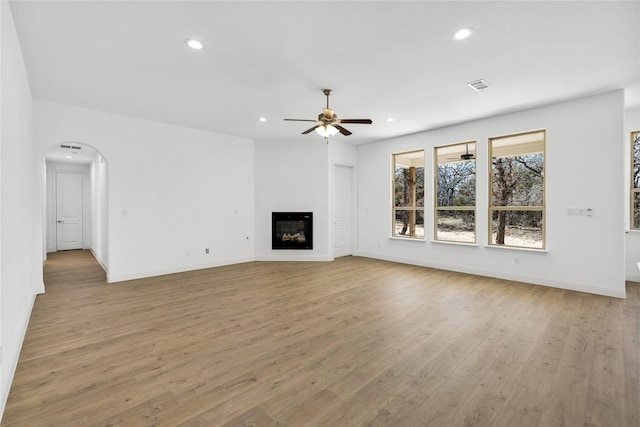 unfurnished living room with visible vents, arched walkways, a glass covered fireplace, wood finished floors, and recessed lighting