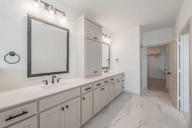 full bathroom with marble finish floor, a sink, a spacious closet, and double vanity