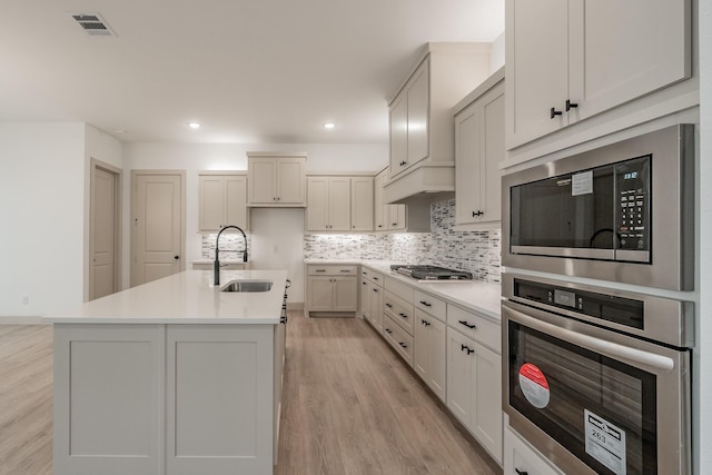 kitchen with a sink, light countertops, appliances with stainless steel finishes, backsplash, and light wood finished floors