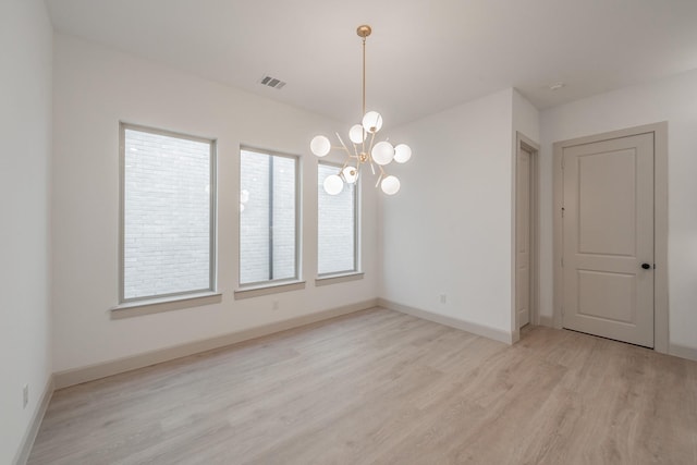 empty room with an inviting chandelier, light wood-style flooring, visible vents, and baseboards