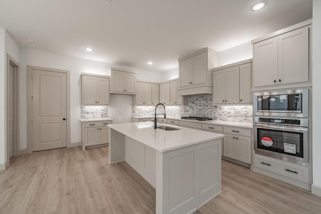 kitchen with light wood finished floors, decorative backsplash, appliances with stainless steel finishes, light countertops, and a sink