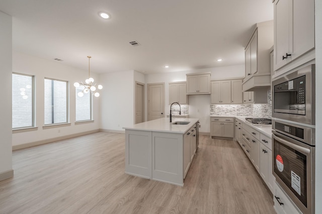 kitchen featuring light wood-type flooring, appliances with stainless steel finishes, decorative backsplash, and a sink