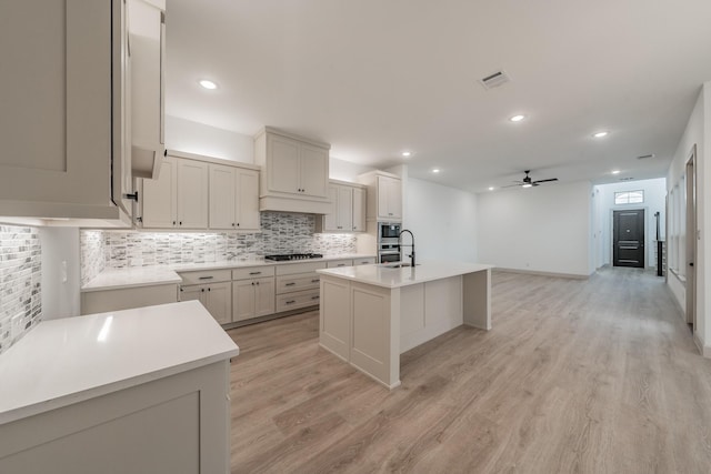 kitchen with a sink, gas stovetop, visible vents, light wood-type flooring, and backsplash