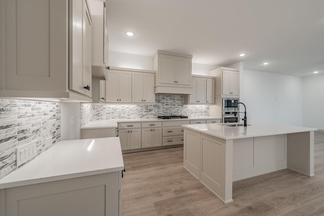 kitchen featuring light wood finished floors, gas stovetop, a kitchen island with sink, and a sink