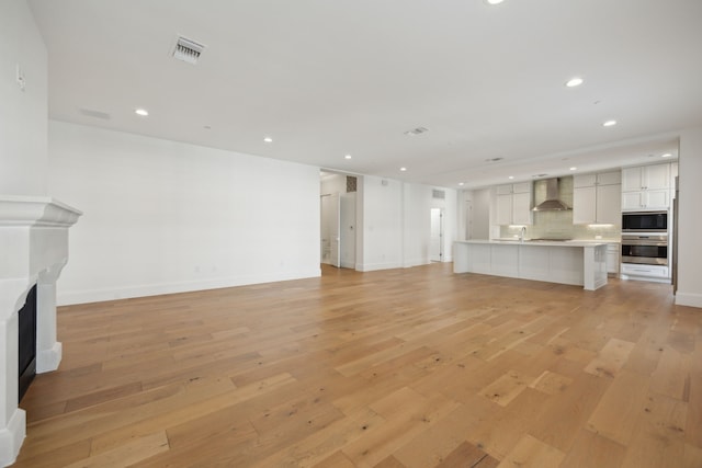 unfurnished living room featuring baseboards, a fireplace, light wood-style flooring, and recessed lighting