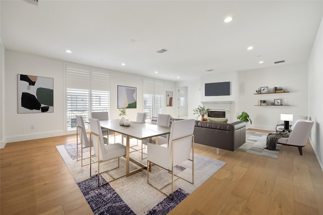 dining space featuring light wood-type flooring, recessed lighting, baseboards, and a glass covered fireplace