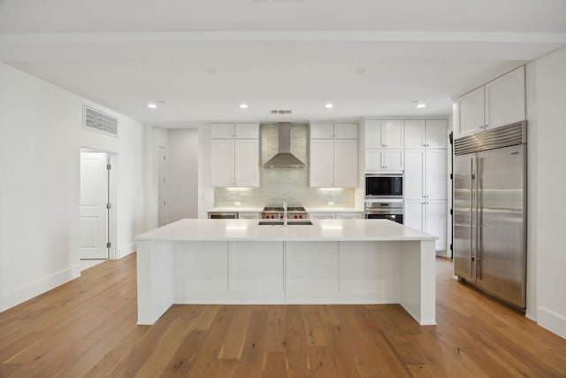 kitchen with built in appliances, a sink, visible vents, light wood-style floors, and wall chimney exhaust hood